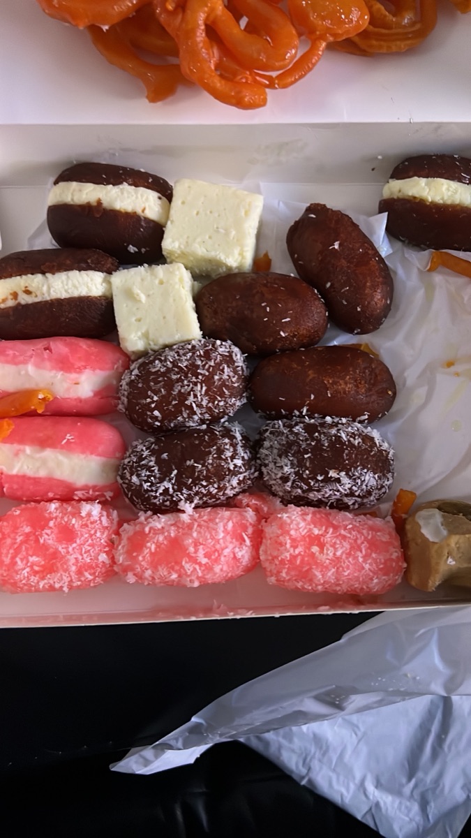 Close-up of Pakistani sweets — jalebi, coconut-rolled gulab jamun, barfi and pink coconut sweets