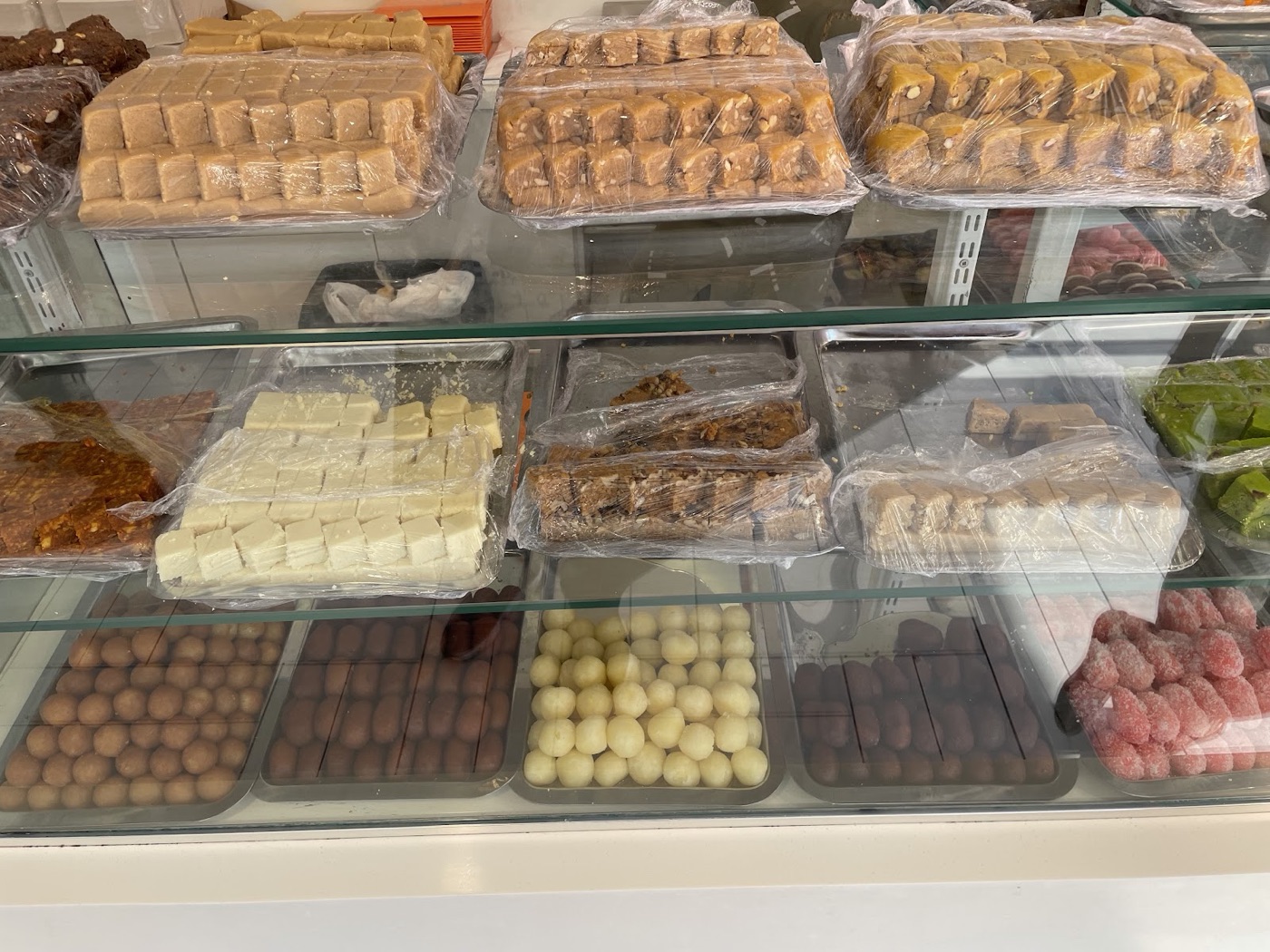 The sweet display case at Original Gourmet with trays of barfi, halwa and coloured dragees